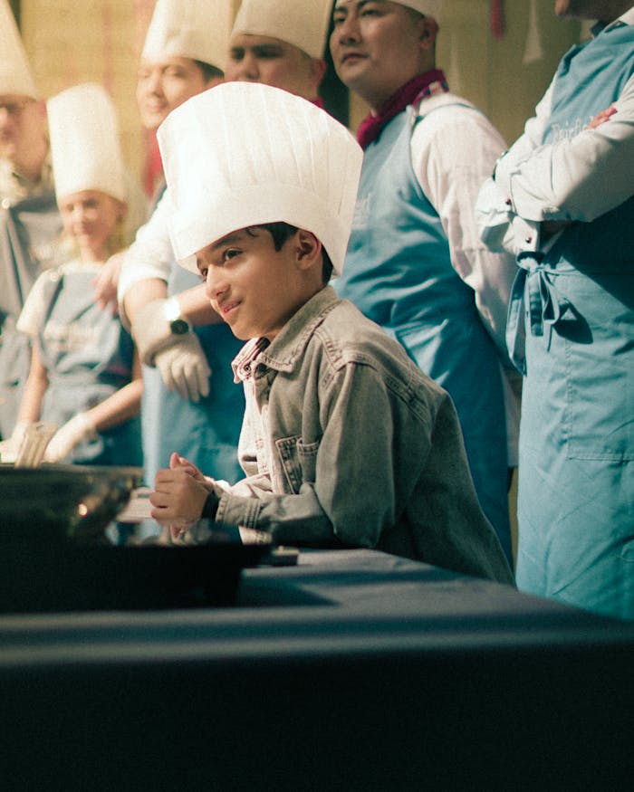A young boy in a chef hat participates in a lively cooking class with instructors.