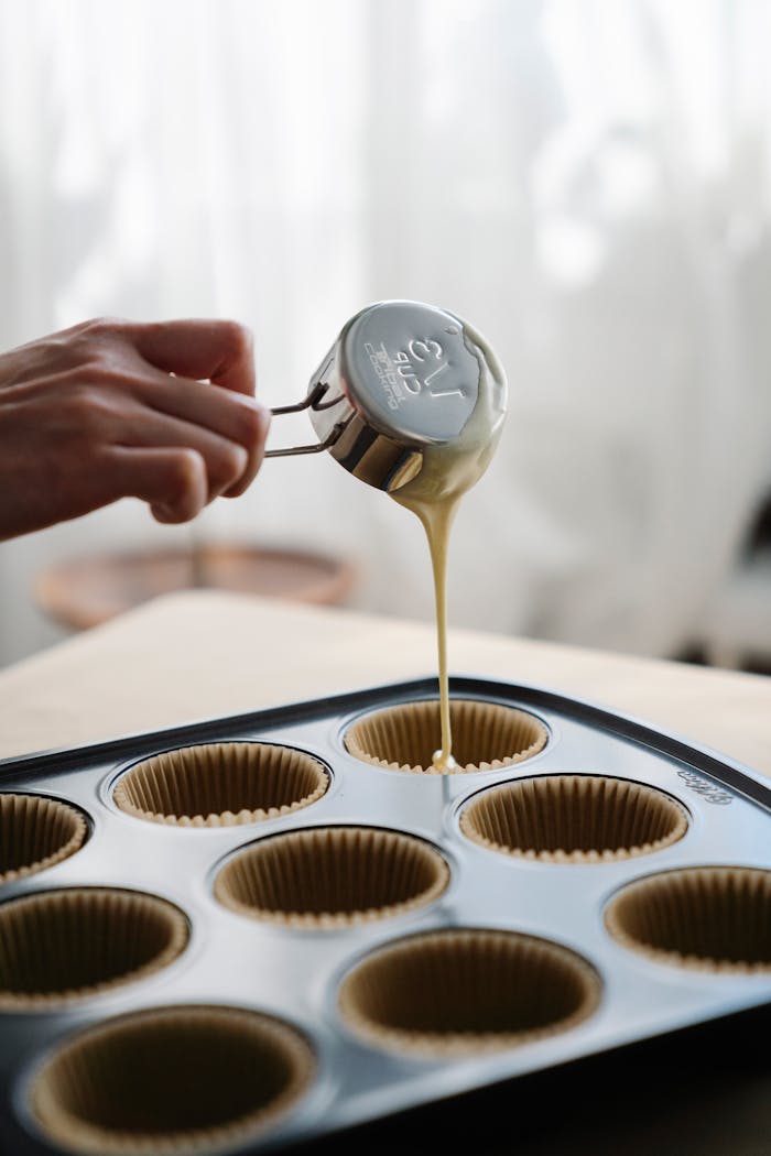 Close-up of pouring batter into muffin liners on a baking tray, indicating homemade baking.